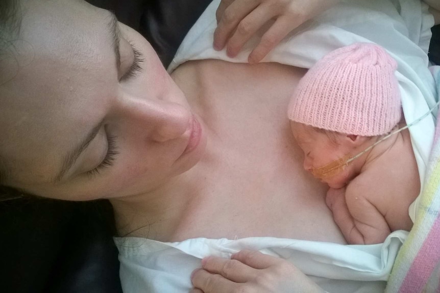 A tiny baby is tucked up on her mother's chest.