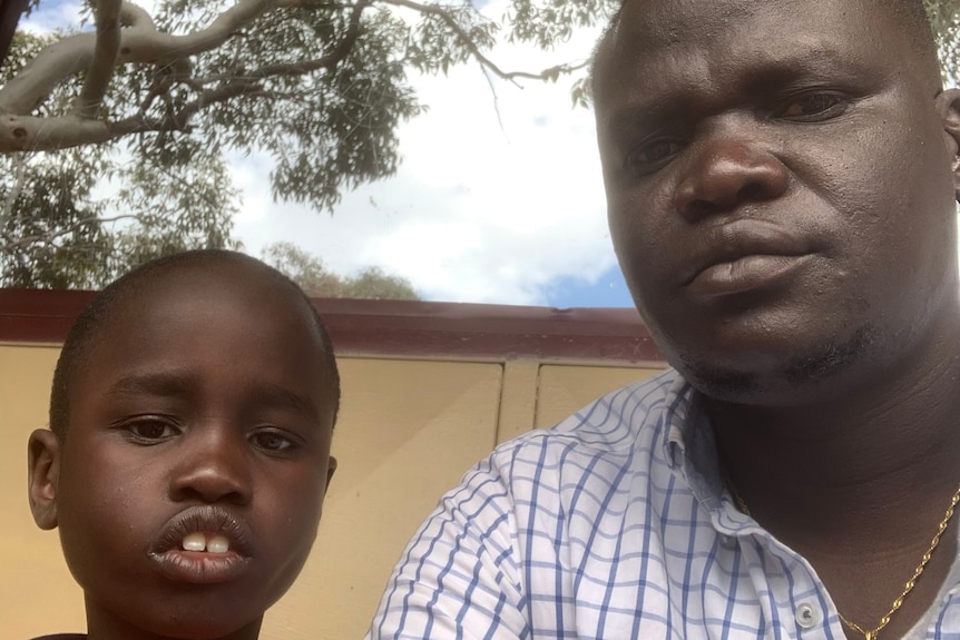 A young boy looks at the camera with his father on the right, taking a selfie