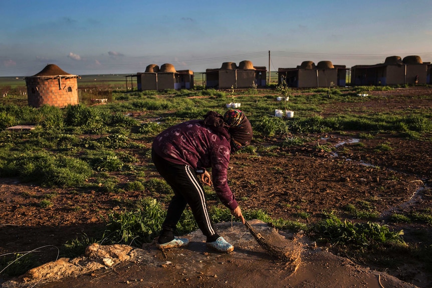 A woman sweeps outside in front of a field