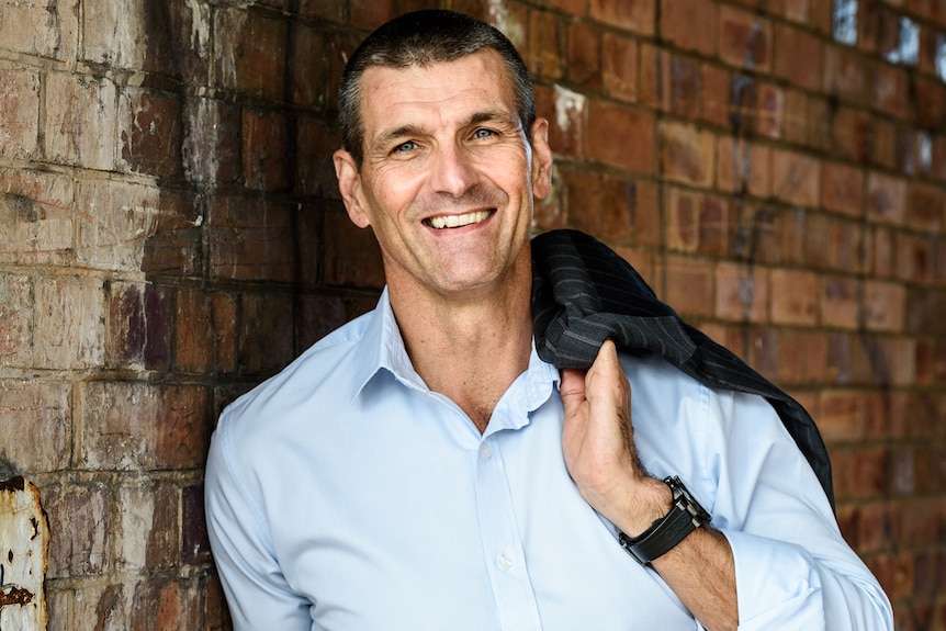 A man stands smiling with a jacket over his shoulder.