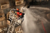 An aerial shot of firefighters in red helmets spraying water from a hose as they stand on a cherry picker.