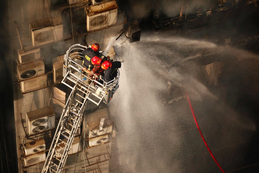 An aerial shot of firefighters in red helmets spraying water from a hose as they stand on a cherry picker.
