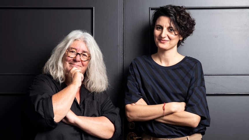 Left: Juliana Engberg, white hair, glasses, shorter, arms folded. Right: Angelica Mesiti, short dark wavy hair, arms folded.