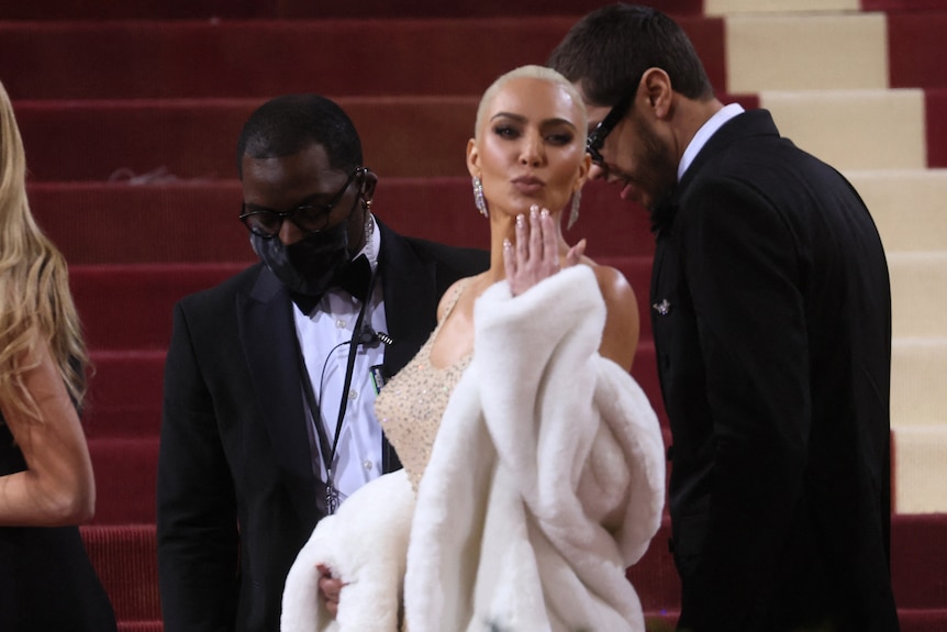 A woman in a silk dress and a white fur coat blows a kiss