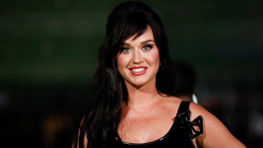 Singer Katy Perry with long dark hair and a black formal dress smiling