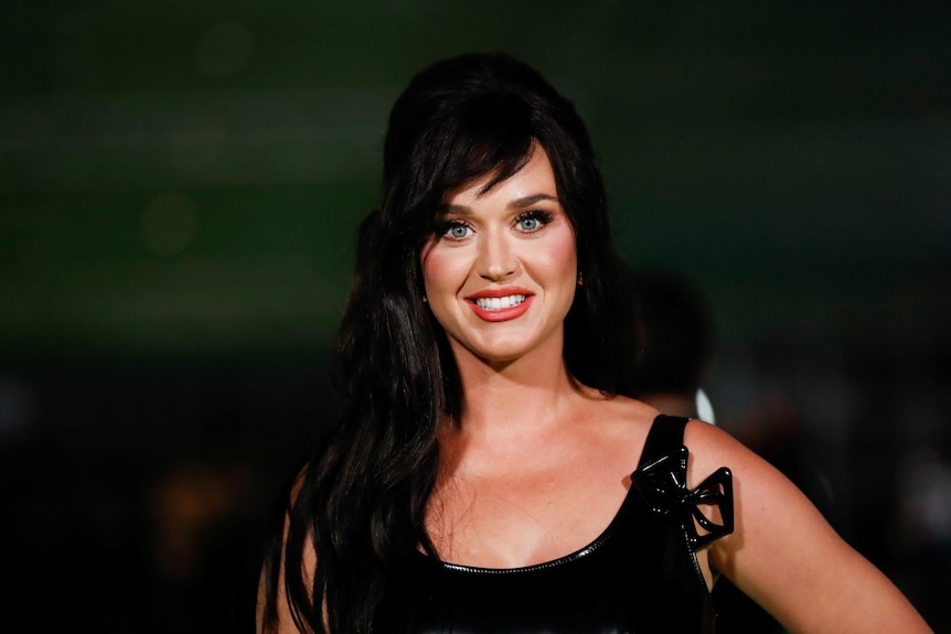 Singer Katy Perry with long dark hair and a black formal dress smiling
