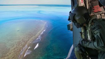 An Australian naval officer looks down from a plane over a reef.