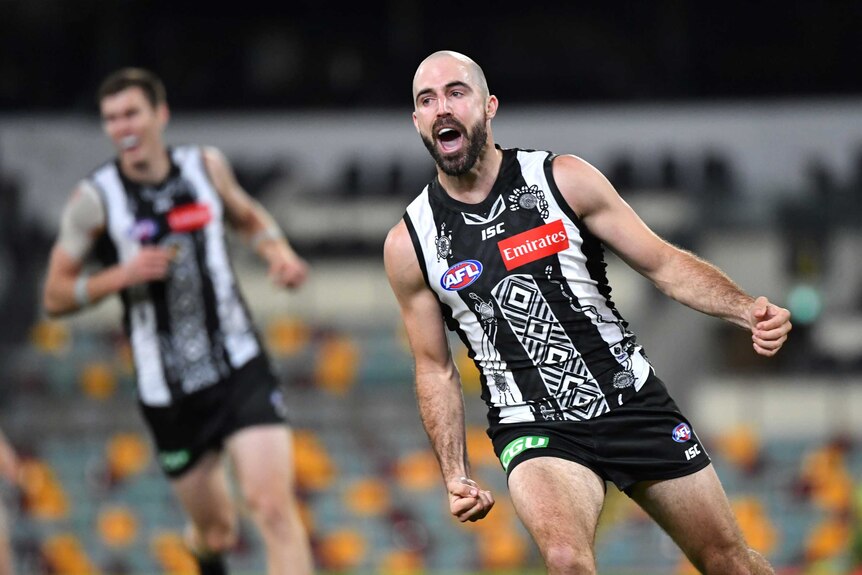 An AFL player wheels away in celebration with his fists clenched after kicking a goal.