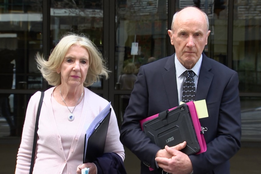 Marg and Brian Moylan hold folders and stare at the camera outside court
