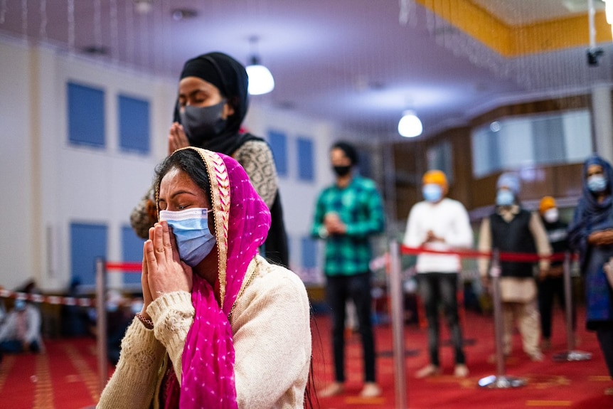 a woman wearing a mask and head covering kneeling and praying