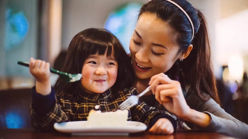 A woman and a young girl eat cake together at a table