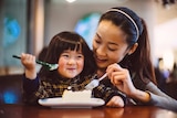 A woman and a young girl eat cake together at a table