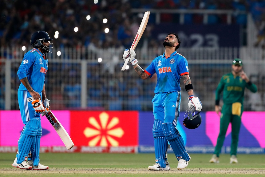 Virat Kohli holds his bat up and looks skyward in celebration of a century