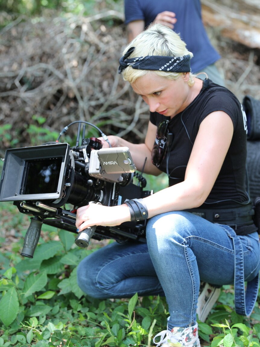 cinematographer halyna hutchins crouches on the ground directing a camera