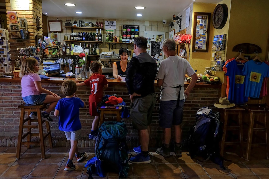 Children and adults lean over a bar in northern Spain, young kids sitting on bistro stools 
