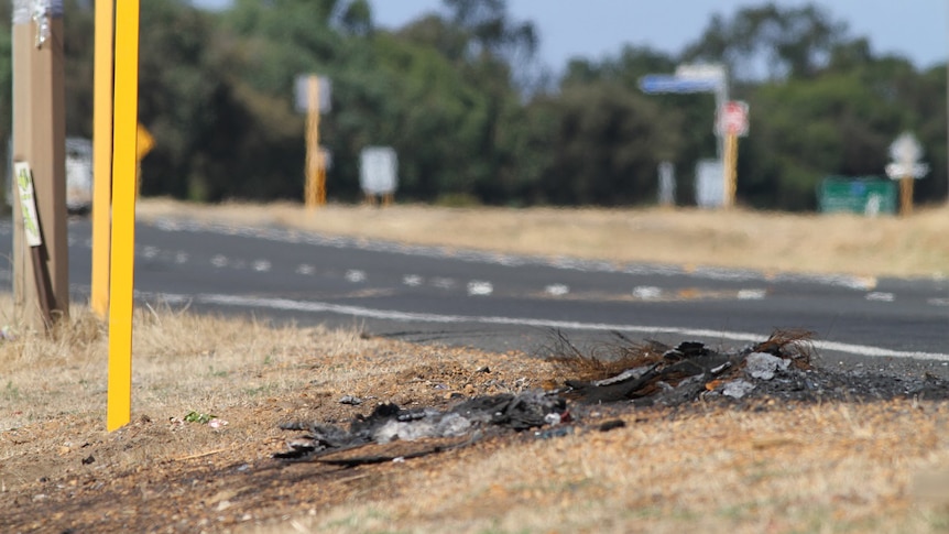 The remains of a burnt-out tyre lie on thr ground on the side of a highway.