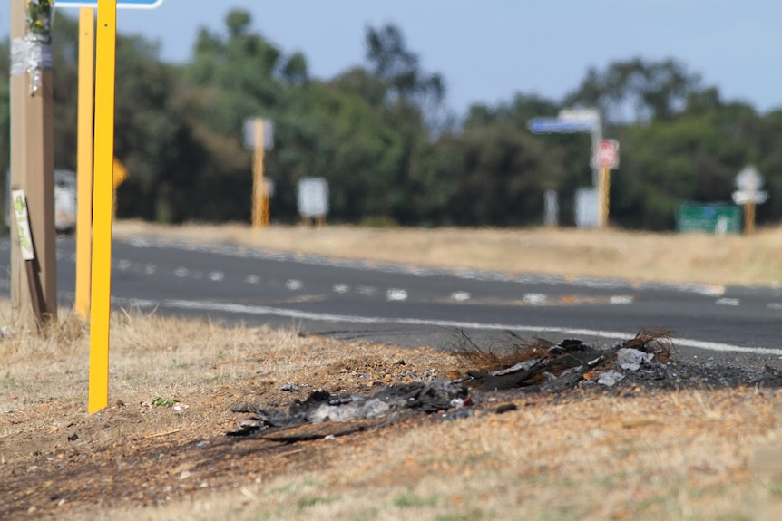 The remains of a burnt-out tyre lie on thr ground on the side of a highway.