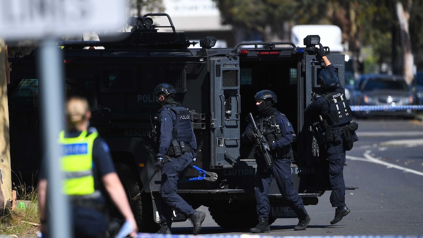 Special operations police exit a black police van next to a crime scene.