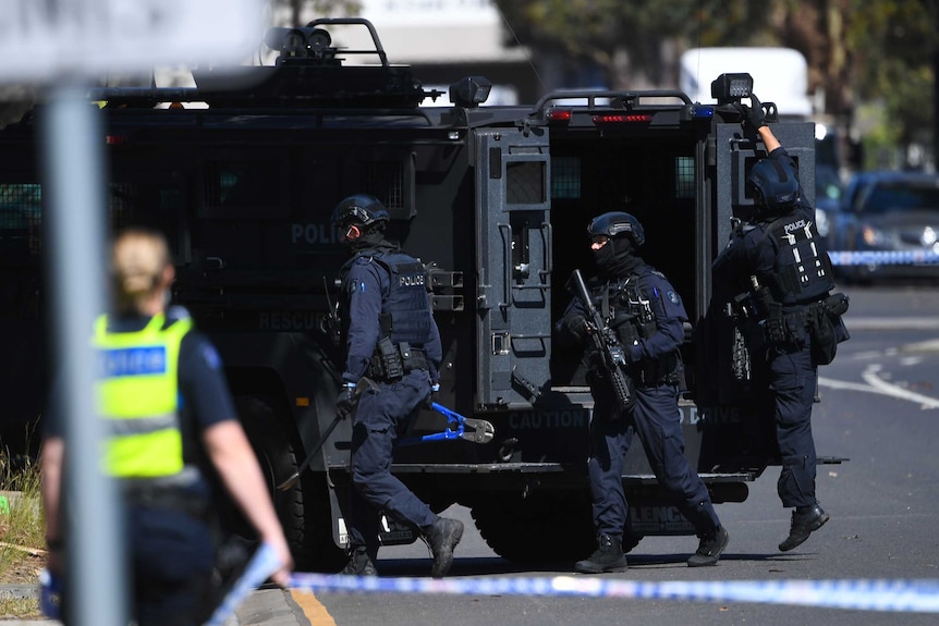 Special operations police exit a black police van next to a crime scene.