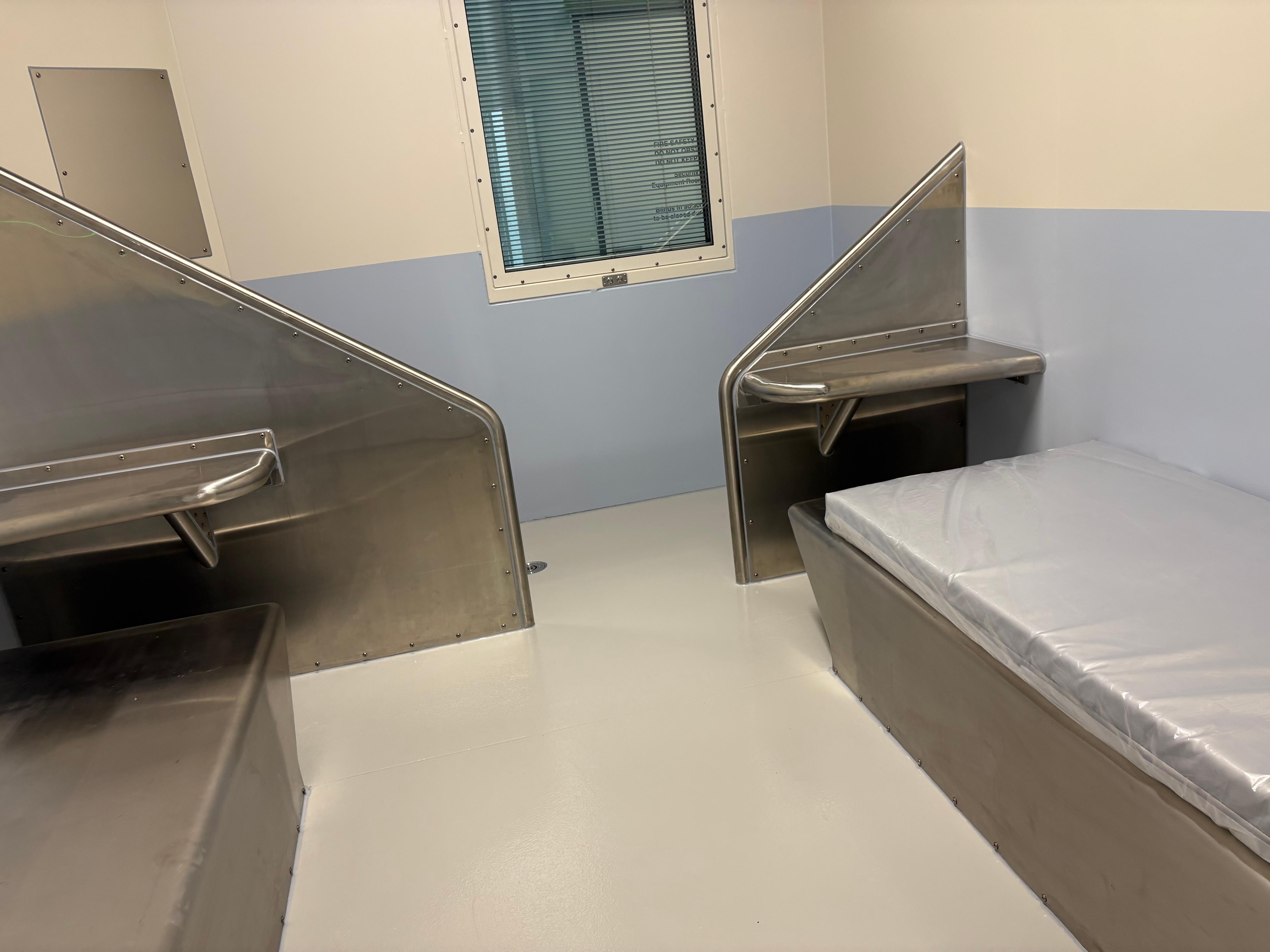 A detention cell with a mattress and metal bench.