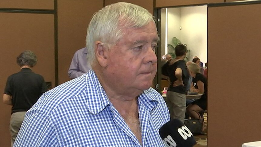 A man with grey hair and a blue checked shirt about to respond to an interview question.