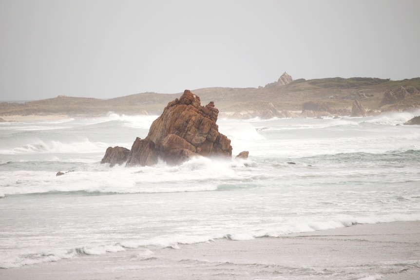 Waves crash around a rocky outcrop in the ocean