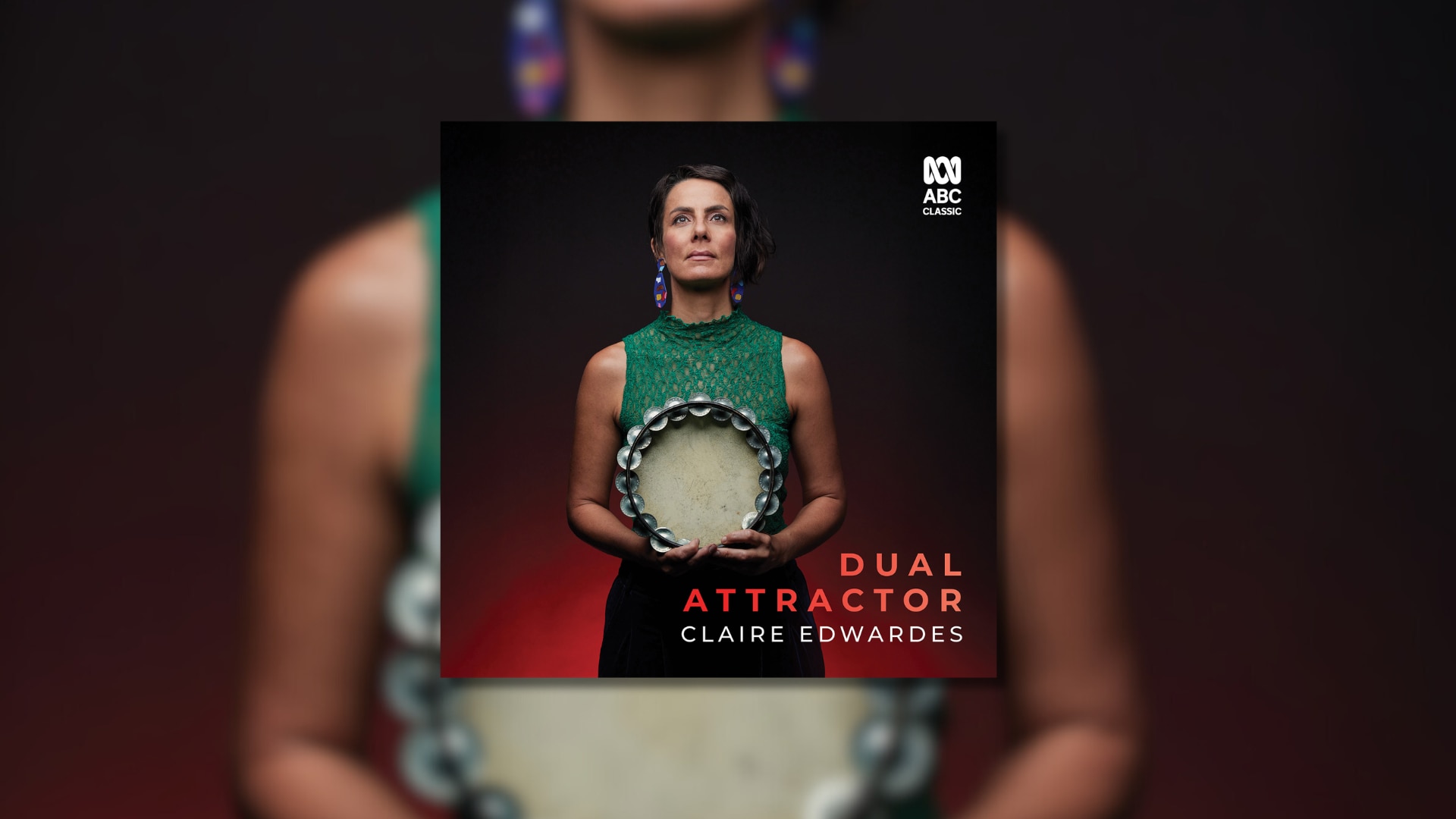 Woman with long colourful earrings in a green tank top holding a tambourine, gazing straight ahead and upwards.