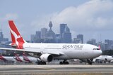 The tail of a Qantas plane is visible through a window at Sydney Airport