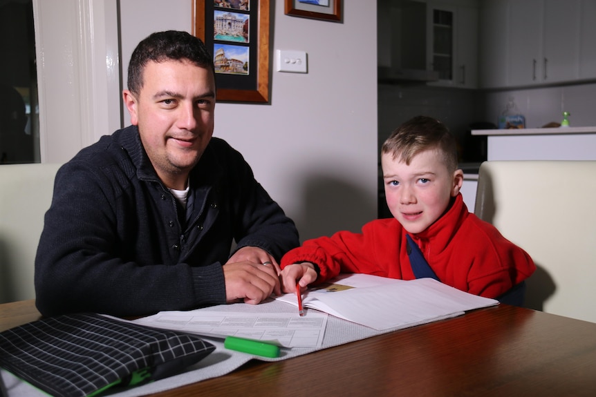 A man wearing a black jumper and a child wearing a red jumper smile at the camera 