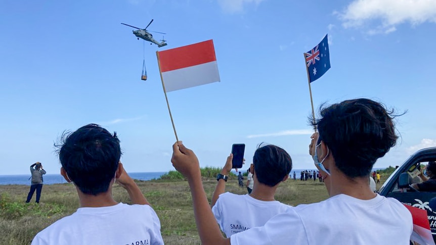 Young people wave Indonesian and Australian flags as a helicopter flies overhead