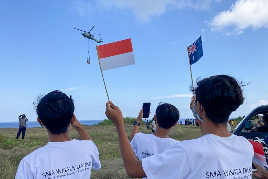 Young people wave Indonesian and Australian flags as a helicopter flies overhead