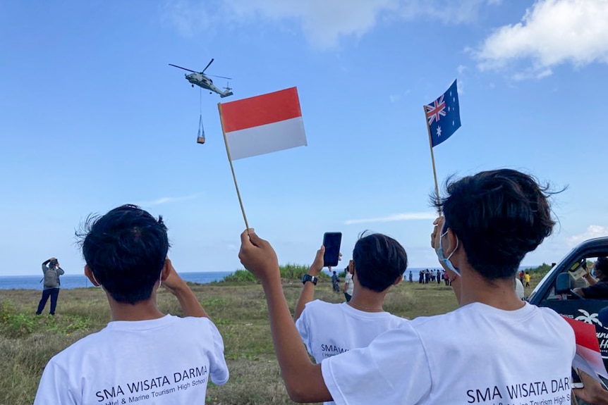 Des jeunes agitent des drapeaux indonésiens et australiens alors qu'un hélicoptère survole