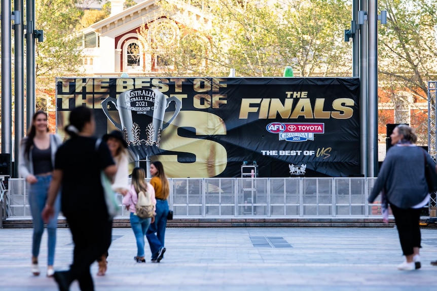 People walking in a city square with an AFL finals banner at the rear.