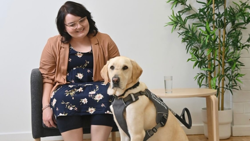 Sarah Maculans sits next to a guide dog.