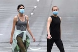 Two women in face masks cross deserted road.