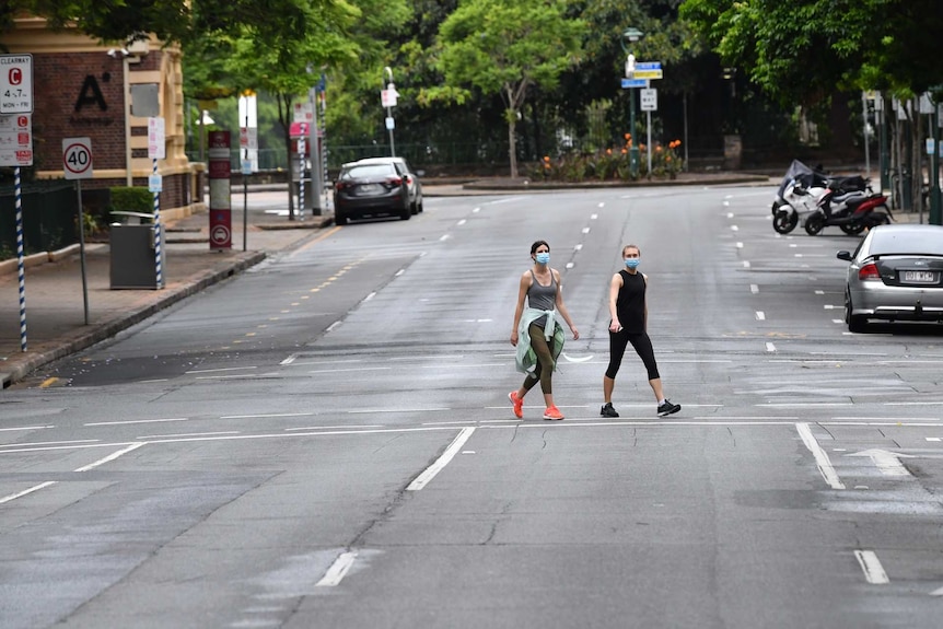 Two women in face masks cross deserted road.