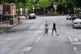 Two women in face masks cross deserted road.
