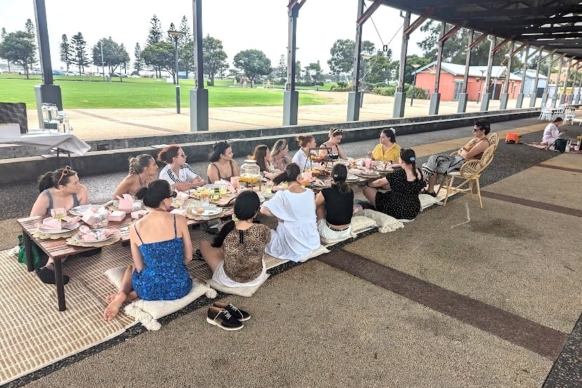 A group of women sit around a table having a picnic. 