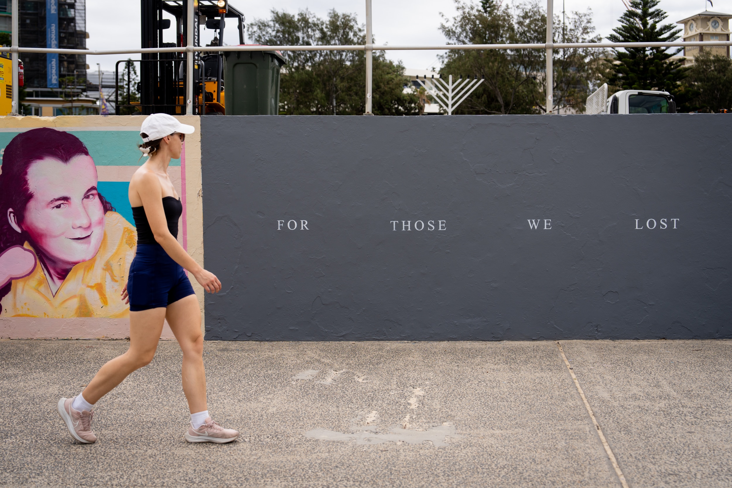Una mujer pasa junto a una pared gris cerca de Bondi que dice 