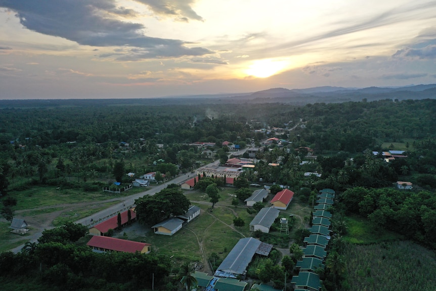 An aerial photo of part of a small village, surrounded by bushland. The afternoon sun is partially covered by cloud.