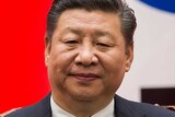 Close-up of Xi Jingping sitting on a chair in front of a red, white and blue background.