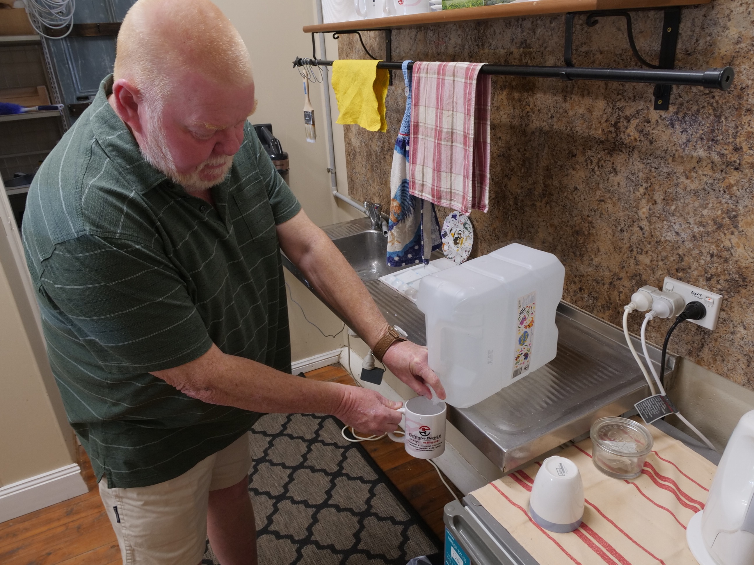 A man pouring water into a cup from a drum 