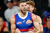 A Western Bulldogs AFL player pumps his fists as he celebrates a goal with a teammate patting him on the back.