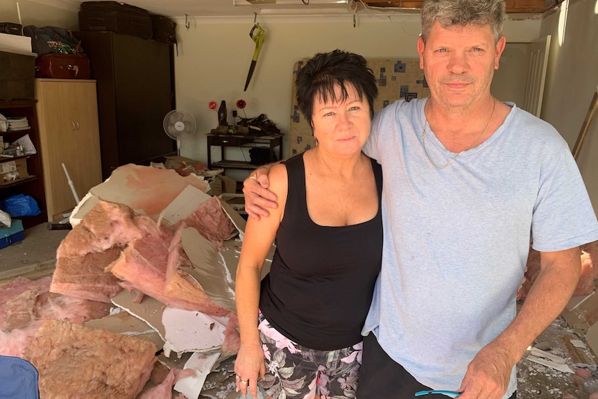 Man and woman stand with arms around each other in damaged home