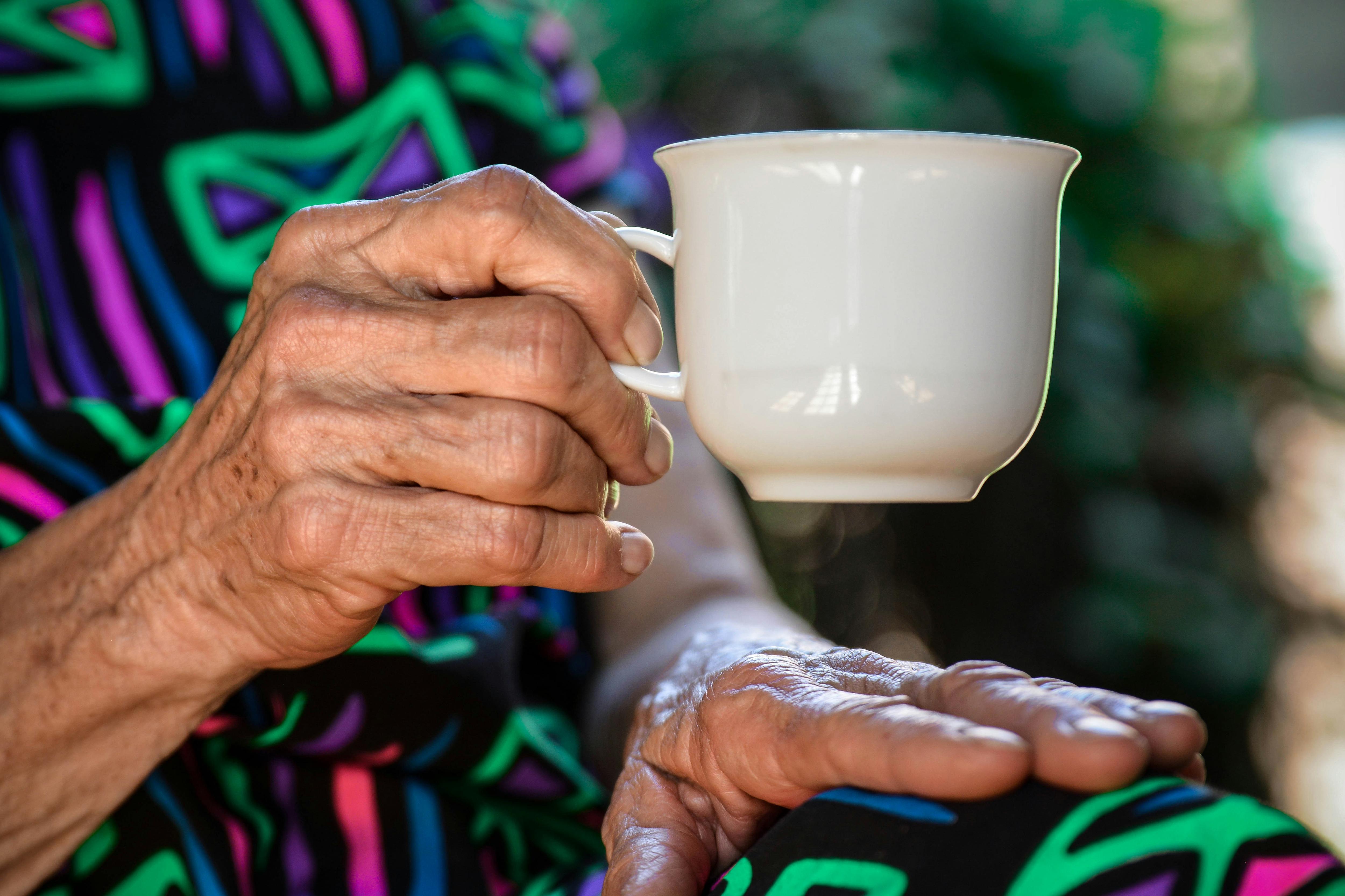 Close up of an elderly woman's hand holding a teacup, with her other hand on her lap. 
