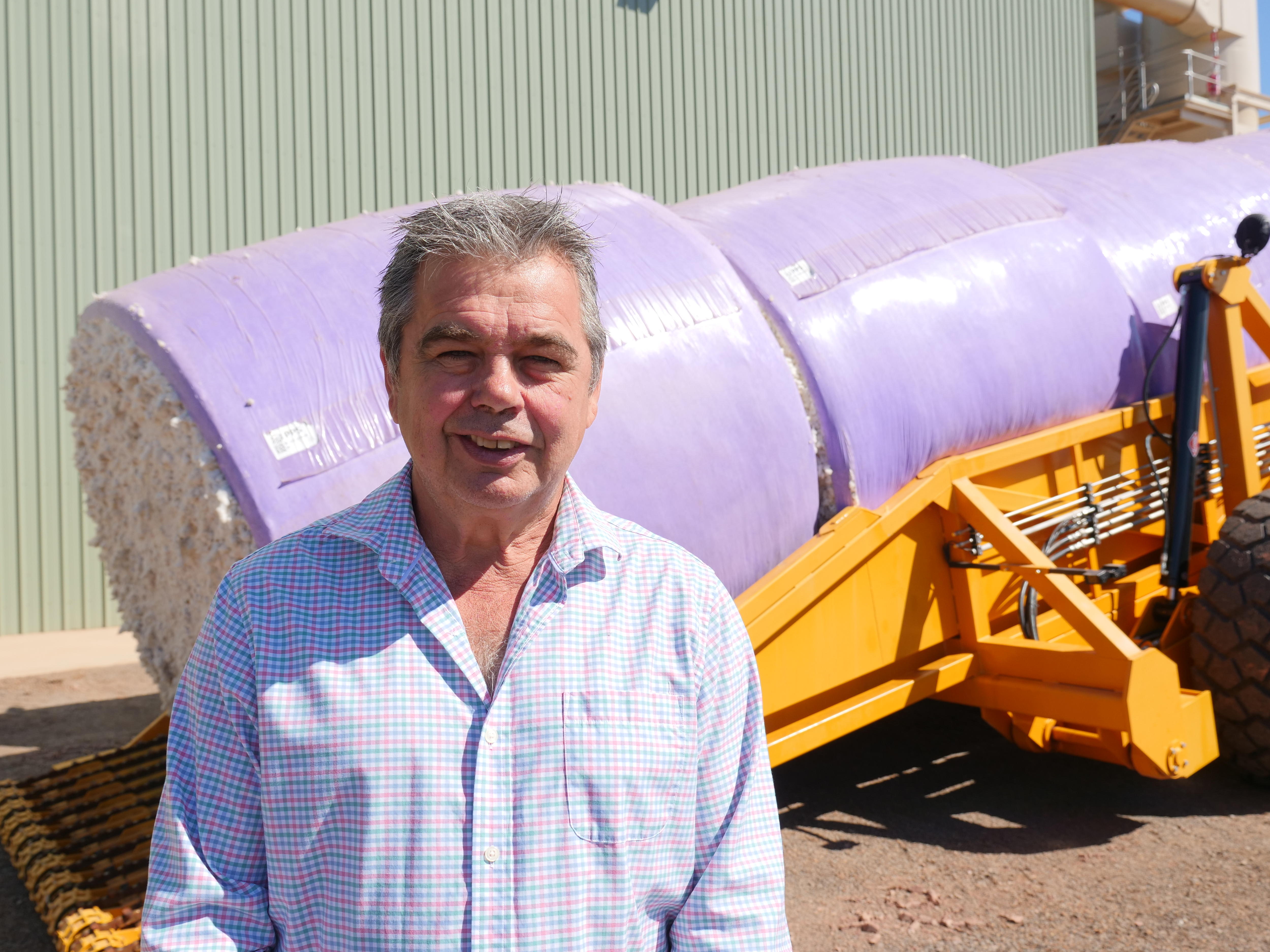 Una foto de retrato de un hombre parado frente al algodón procesado