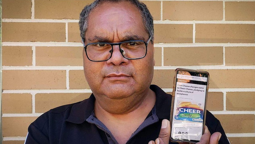 Man who is Indigenous holds a smartphone displaying an article on the change of name of Coon cheese to Cheer cheese.