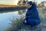 Emerald-based cotton grower Renee Anderson squats next to a body of water.