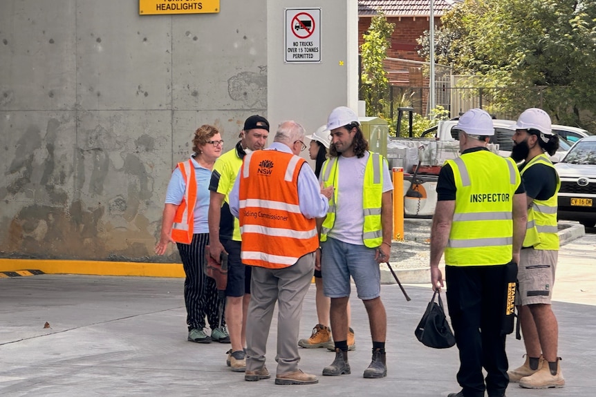 A group of people in hard hats and high-vis stand at a construction site, speaking.