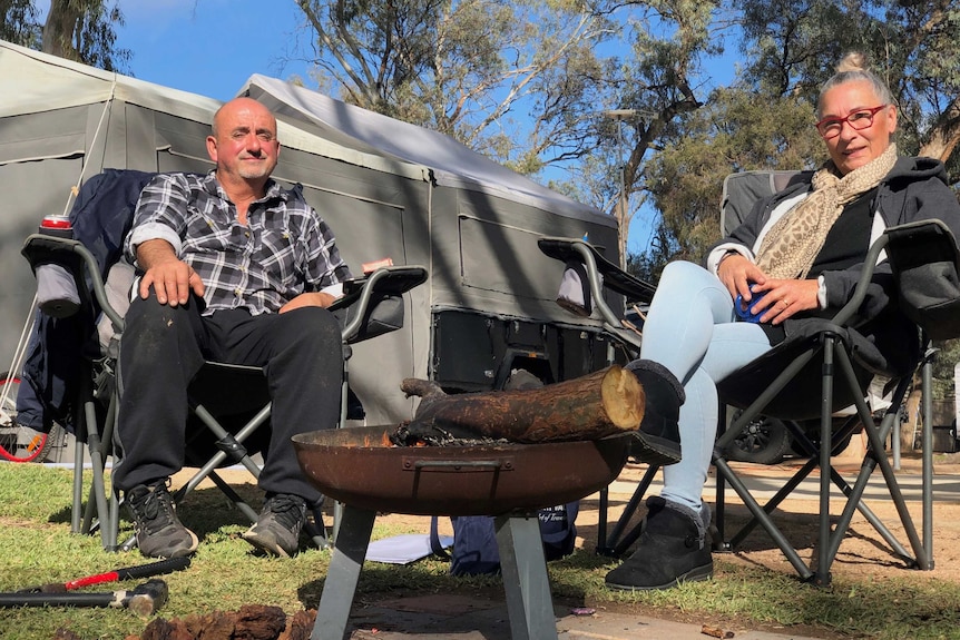 A man and a woman sit in deck chairs by a small camp fire